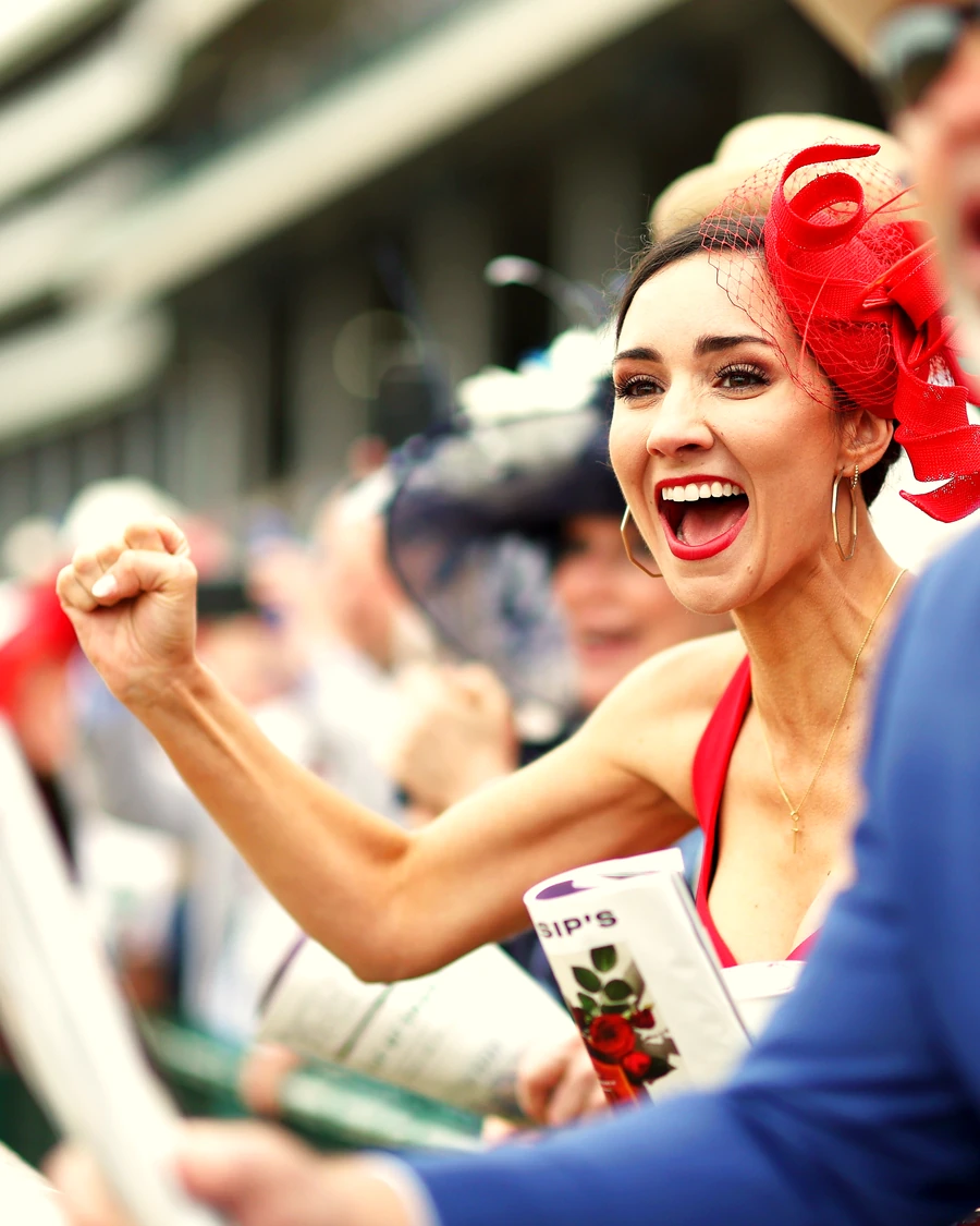 A woman in a red Derby fascinator cheering at the rail